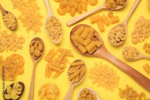 Different types of pasta on yellow background, flat lay photo