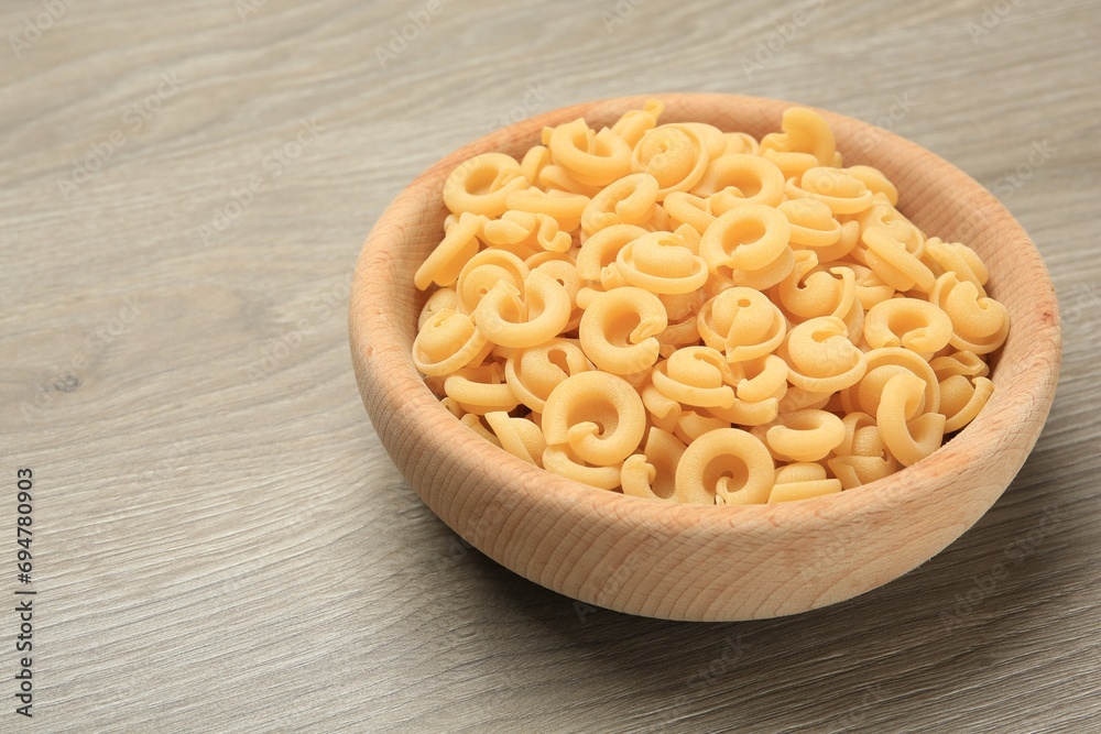 Raw dischi volanti pasta in bowl on light grey wooden table, closeup. Space for text Raw dischi volanti pasta in bowl on light grey wooden table, closeup. Space for text