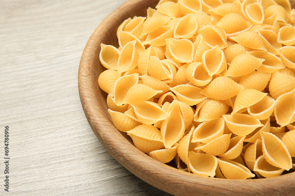 Raw conchiglie pasta in bowl on light grey wooden table, closeup