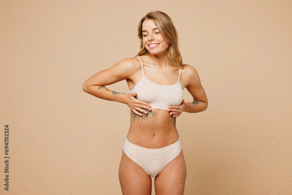 Fototapeta premium Young nice lady woman with slim body perfect skin wear nude top bra lingerie stand put hand on chest cancer early diagnostic isolated on plain pastel light beige background Lifestyle diet fit concept