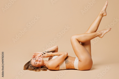 Full body side profile view young nice lady woman with slim body perfect skin wearing nude top bra lingerie lay down raise up legs isolated on plain pastel beige background Lifestyle diet fit concept