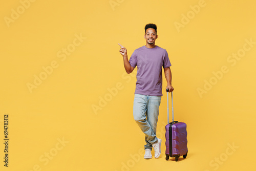 Traveler happy man wears casual clothes hold bag point finger aside isolated on plain yellow background studio. Tourist travel abroad in free spare time rest getaway. Air flight trip journey concept. photo