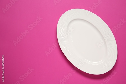 One white plate on pink background, top view. Space for text