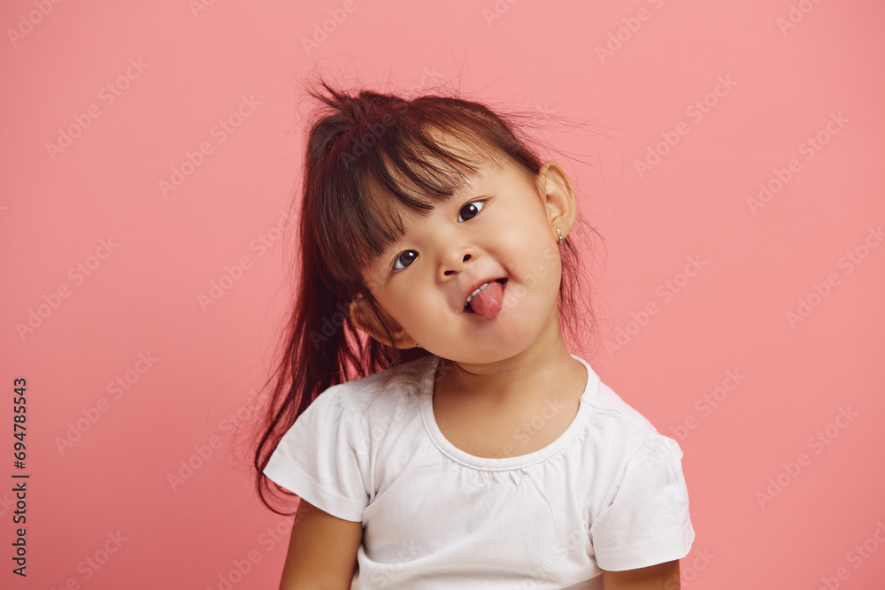 headshot portrait of playful female child tilted her head and shows her tongue standing over a pink isolated background. headshot portrait of playful female child tilted her head and shows her tongue standing over a pink isolated background.