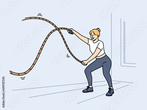 Woman doing fitness using battle rope training at sport center to lose weight or build muscles. Girl athlete with battle rope prepares for competitions and leads healthy lifestyle.