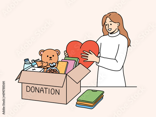 Kind woman stands near donation box with big heart in hands, wanting to help people in need. Collecting donation box of toys and books for children who find themselves in difficult financial situation