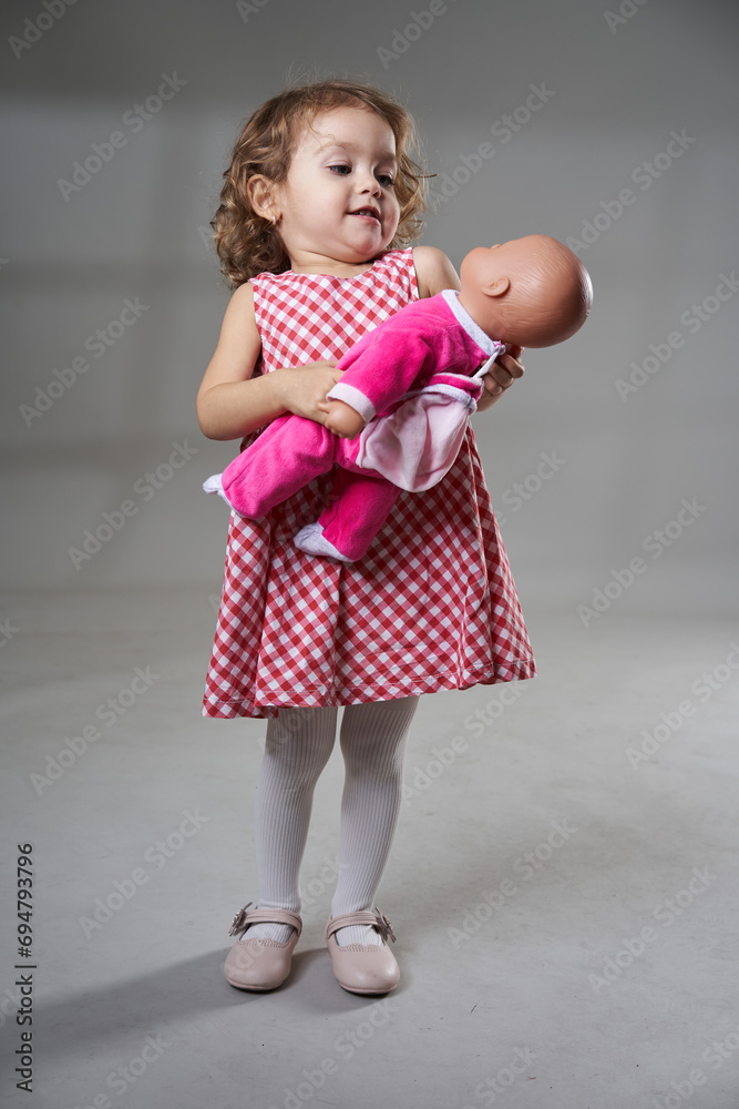 Adorable blonde little girl with a doll on gray background