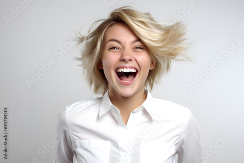 Portrait of a happy young blonde woman in a white shirt on a gray background