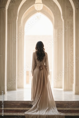 Rear view of a slender woman wearing a long dress against the background of a mosque, a beautiful building.