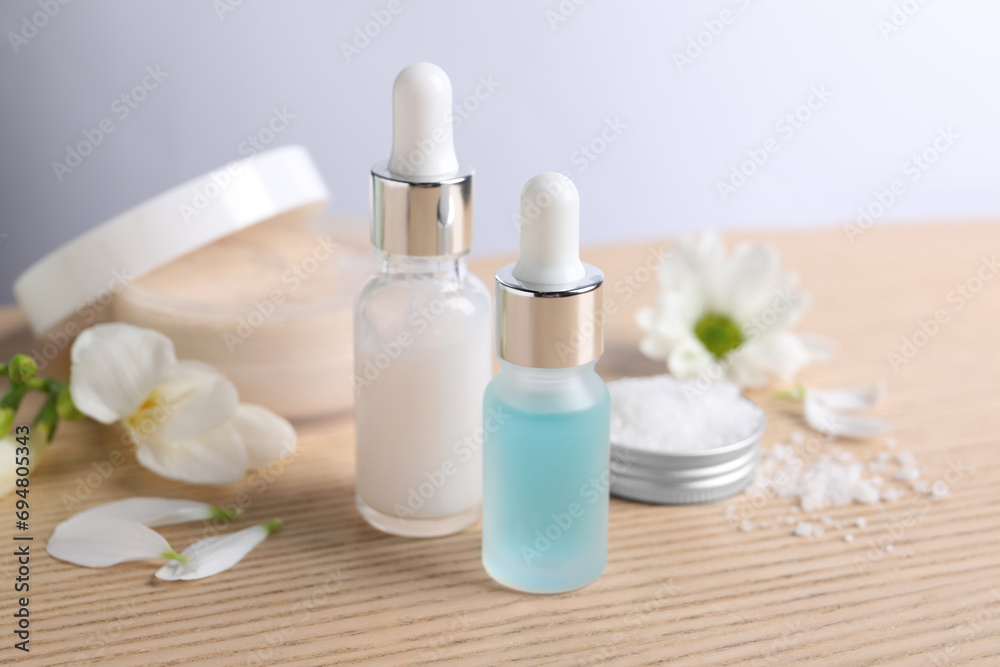 Bottles of cosmetic serum and beautiful flowers on wooden table, closeup