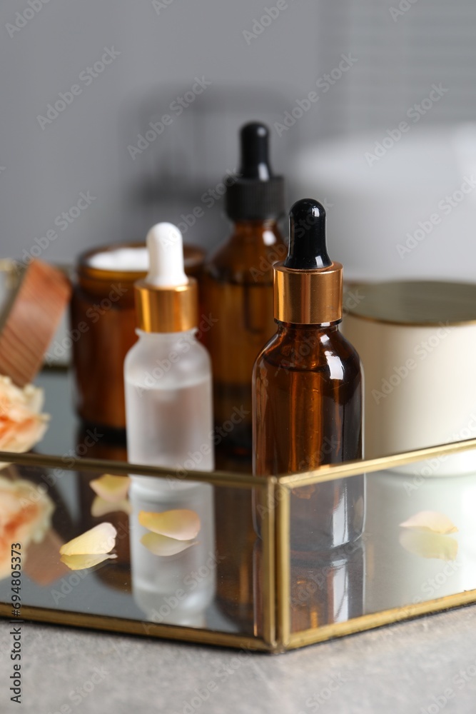 Bottles of cosmetic serum and beauty products on gray table, closeup