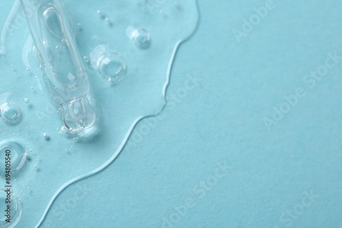 Dripping cosmetic serum from pipette onto light blue background, above view. Space for text photo