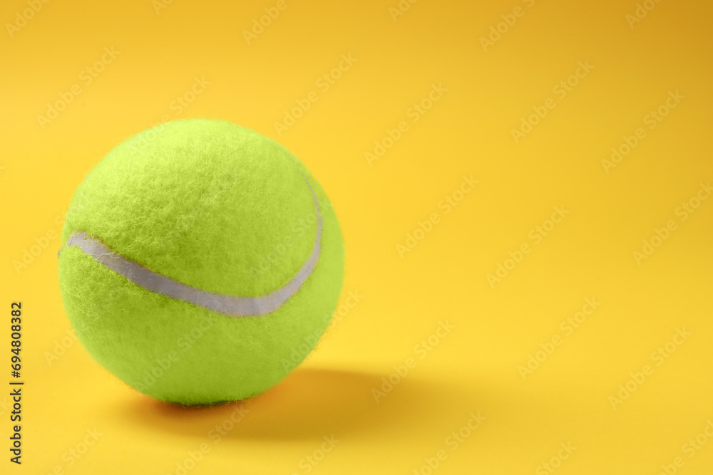 One tennis ball on yellow background, space for text