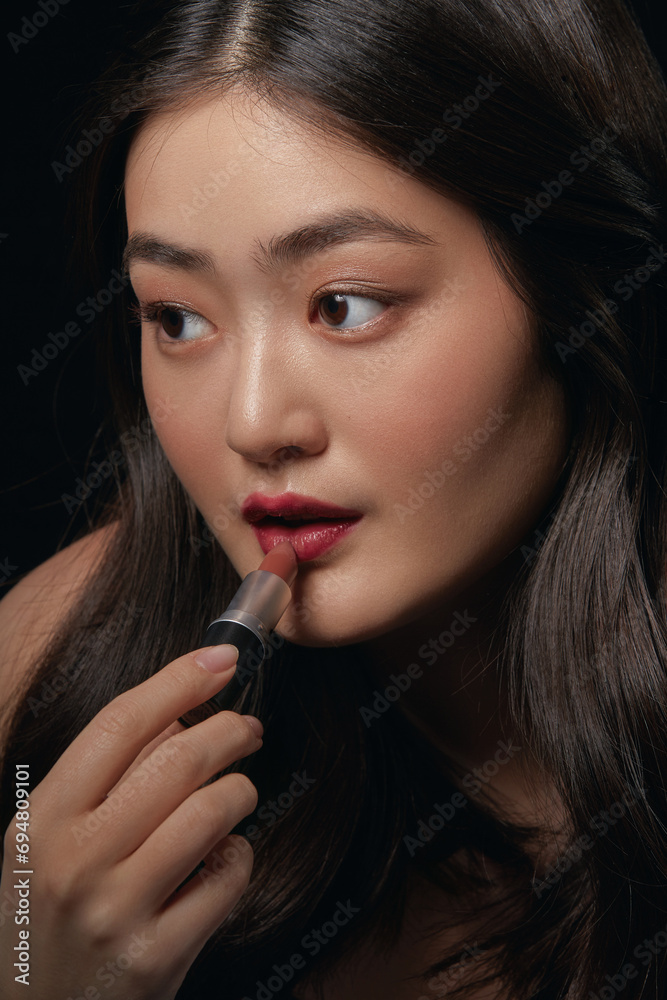 Attractive and sensual asian woman applies red lipstick over black background. Cosmetic, make up and beauty concept. Attractive and sensual asian woman applies red lipstick over black background. Cosmetic, make up and beauty concept.