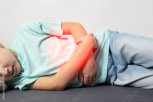 A seven-year-old girl in a green T-shirt lies and holds her stomach with her hands. Stomach pain in children. Esophagitis and gastroduodenitis. Diseases of the gastrointestinal tract in children photo