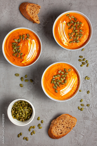 Three plates of pumpkin soup with seeds, sour cream, spices on a gray background