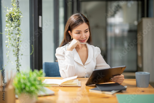 Asian business woman working using a digital tablet. Think, analyze data and plan work. Record in a notebook.