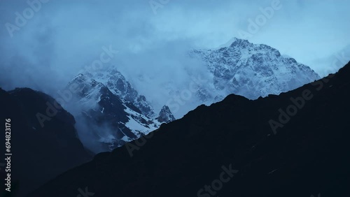 A beautiful timelapse shot of the cloudy and snowy Himalayan mountains behind the Kedarnath temple in Uttarakhand, India. photo