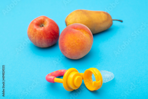 Apple, pear and peach with baby nibbler on a blue background. Concept of feeding fruits and vitamins to babies. Development of the chewing reflex in children, close-up photo