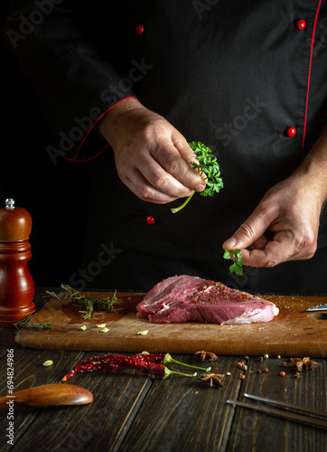 The cook adds aromatic parsley to the meat steak for a delicious taste. The concept of cooking veal shish kebab on the kitchen table.