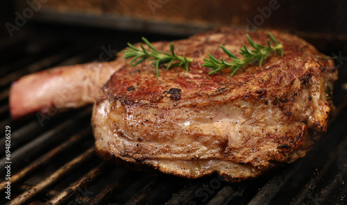 A single ribeye steak on the bone with rosemary herb garnish cooking on the bbq or barbecue grill. The prefect cut of beef meat close up cooking on the griller. photo