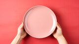 Top view of female hands holding pink empty plate on red background.