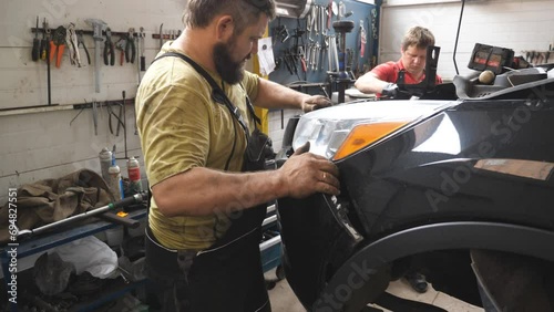 Two mechanics removing front bumper from car for repair in auto service. Professional repairmans dismantling automobile before fix at workshop or garage. Concept of vehicle maintenance and diagnostic photo
