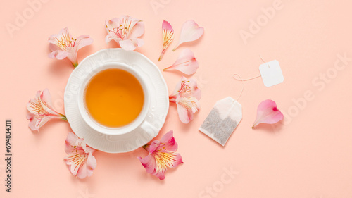 Cup of tea with flowers and tea bag with white empty label on pink background, top view, banner size. Fruit natural aroma tea with teabag