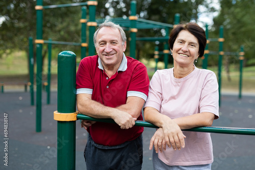 Portrait of an elderly couple in sportswear on sports ground in a city park on summer day