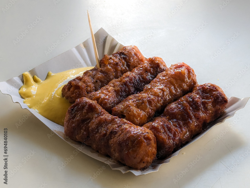 Mici with mustard and a toothpick on a paper plate. Traditional romanian fast food.