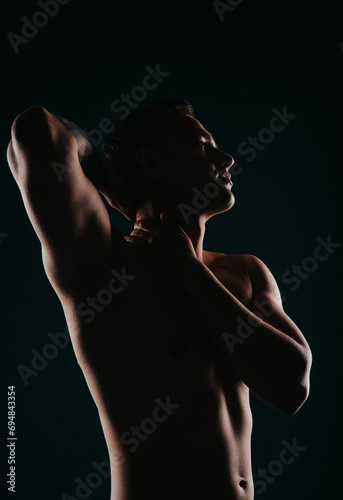 An active man showcases his strong and muscular body transformation, flexing muscles and showing off his six pack in a silhouette on a black background.