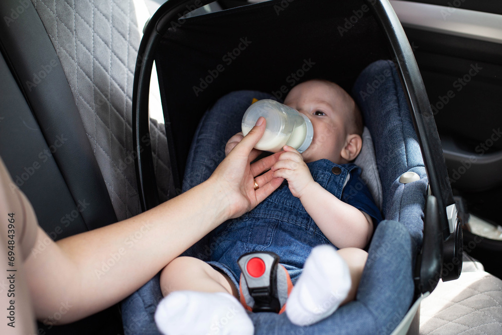 mother feeds the baby in, car seat in the car, milk from a bottle. Feeding children in car seats, close-up mother feeds the baby in, car seat in the car, milk from a bottle. Feeding children in car seats, close-up