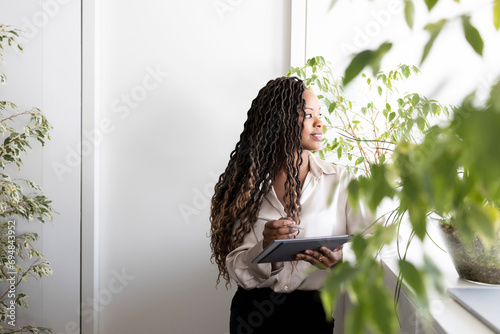 Thoughtful businesswoman holding digital tablet and stylus in office photo
