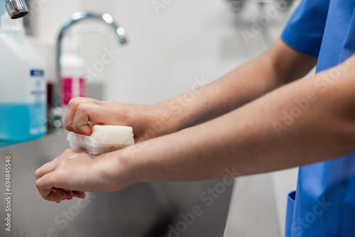 Crop nurse washing hands with sponge in sink at hospital photo