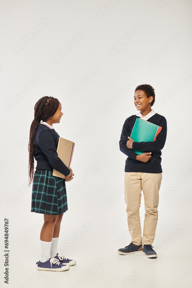 happy african american kids in neat school uniform holding textbooks and standing on grey backdrop happy african american kids in neat school uniform holding textbooks and standing on grey backdrop