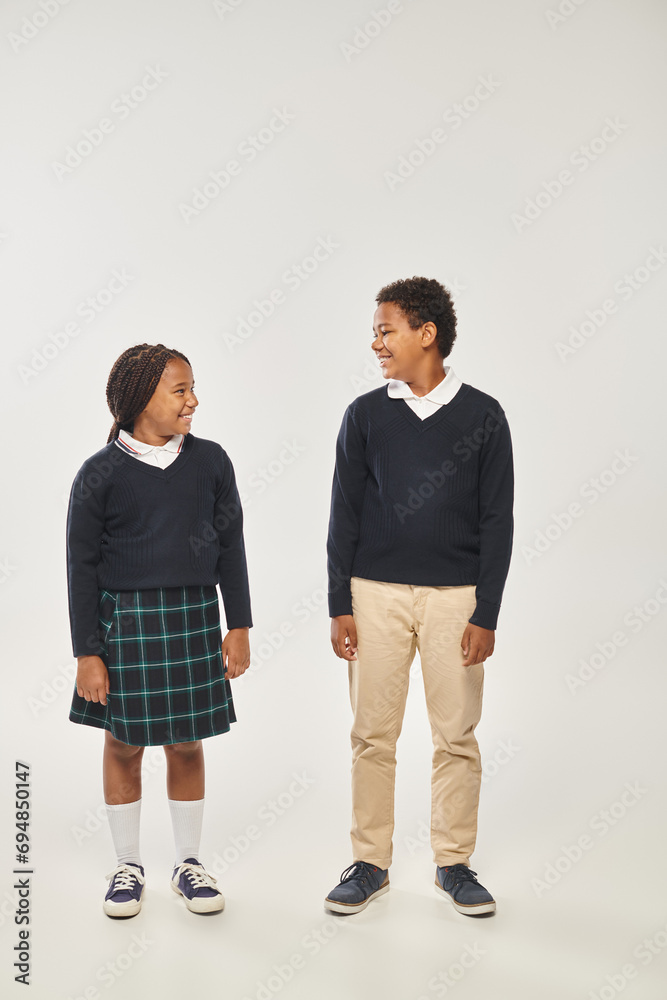 cheerful african american schoolchildren in uniform smiling at each other on gray background cheerful african american schoolchildren in uniform smiling at each other on gray background