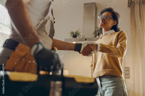 Close up of male handyman shaking hands with happy female client while standing at home kitchen