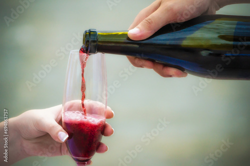 man pours red wine from a bottle into a glass in a woman's hand photo
