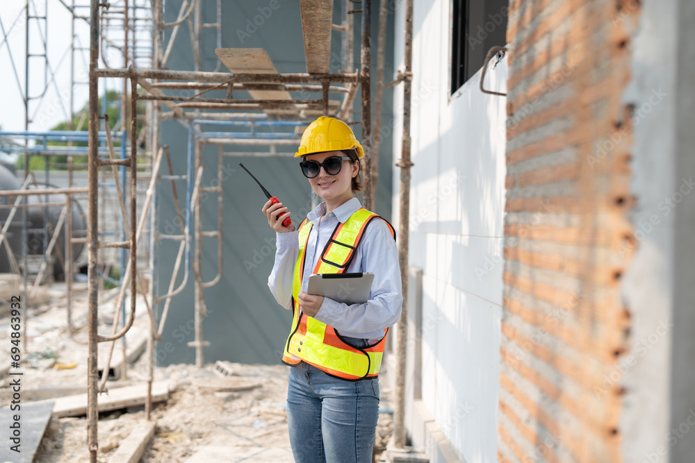 Civil female engineer holding blueprints and using radio talking instructing and inspection building progress on construction site. Civil female engineer holding blueprints and using radio talking instructing and inspection building progress on construction site.