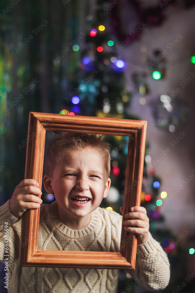 portrait of a cute boy of European appearance in a wooden picture frame against the backdrop of a Christmas tree in the room