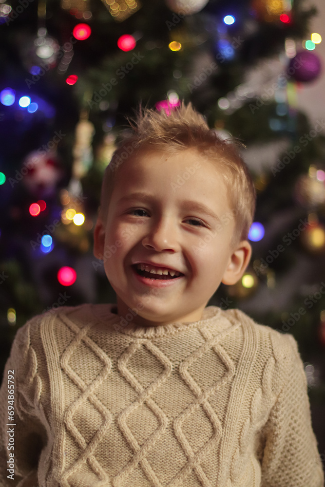 close-up portrait of a boy in a sweater against the background of a blurry Christmas tree close-up portrait of a boy in a sweater against the background of a blurry Christmas tree