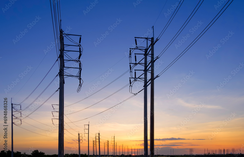 Silhouette two rows of many electric poles with cable lines in countryside area against beautiful sunset sky background in evening time, perspective low angle view