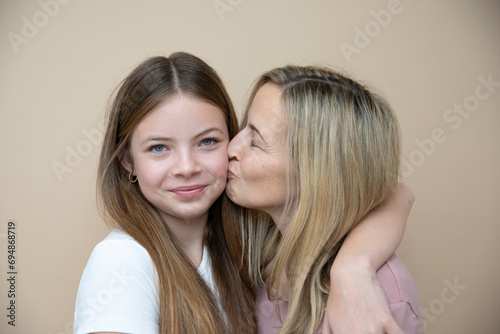 beautiful young, teenager girl together with her beautiful mother posing in front of brown background