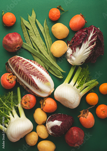 Fototapeta Naklejka Na Ścianę i Meble -  December winter vegetables and fruits on a green background: fennel, radicchio, persimmon, potatoes and tangerines and pomegranate. Seasonal healthy food