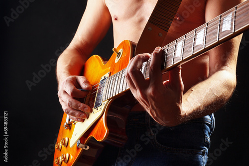 Artist plays the orange sunburst electric guitar on dark stage.