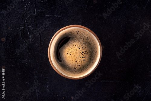 A cup of black coffee with froth, overhead flat lay shot on a dark background