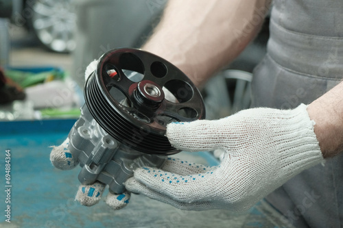 The power steering pump.Close-up.An auto mechanic checks the serviceability and compliance of a spare part before replacing it during car repair at a service station.