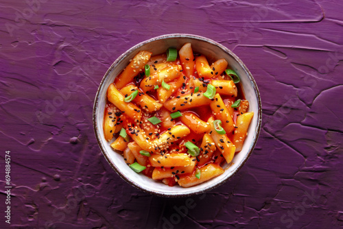 Tteokbokki or topokki, Korean street food, spicy rice cakes in red pepper gochujang sauce, overhead flat lay shot on a purple background photo