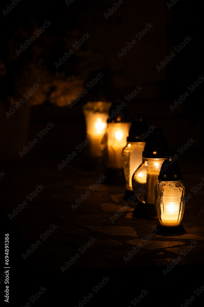 Night shot of the flames of glass cemetery candles standing on tombstones. The shot was taken during All Saints' Day, November 1. Night shot of the flames of glass cemetery candles standing on tombstones. The shot was taken during All Saints' Day, November 1.