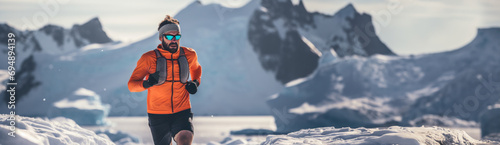 Young athletic man in sportswear and goggles running on snowy mountains. Banner. Concept of cross-country run, marathon, endurance, competition photo